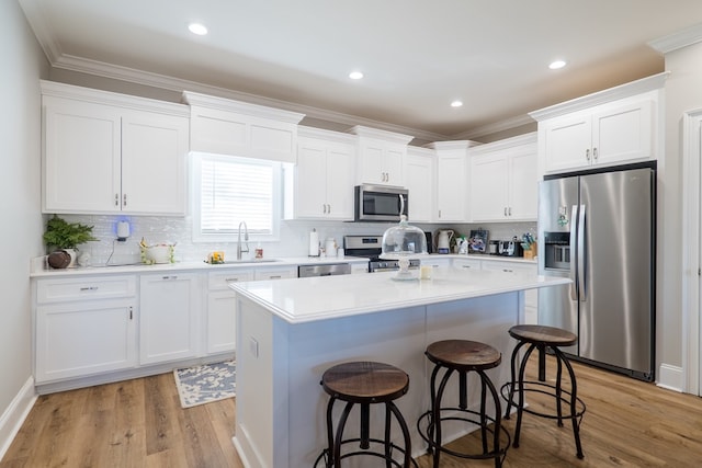 kitchen featuring light wood-type flooring, stainless steel appliances, sink, white cabinets, and a kitchen island