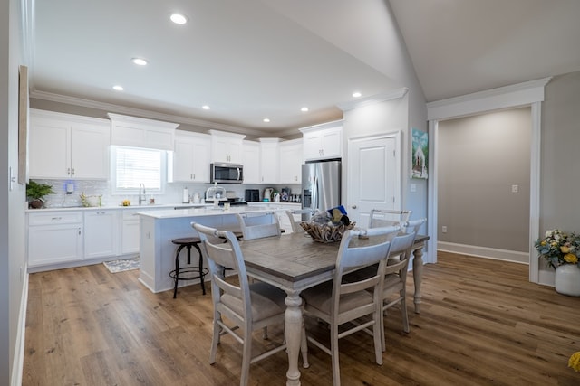 dining room featuring wood-type flooring, vaulted ceiling, crown molding, and sink