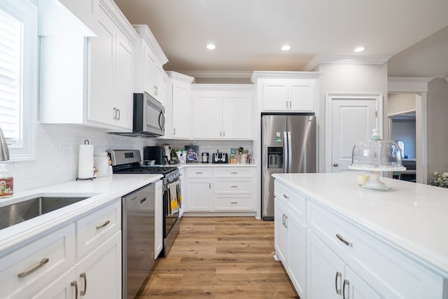 kitchen featuring white cabinetry, light wood-type flooring, decorative backsplash, appliances with stainless steel finishes, and ornamental molding