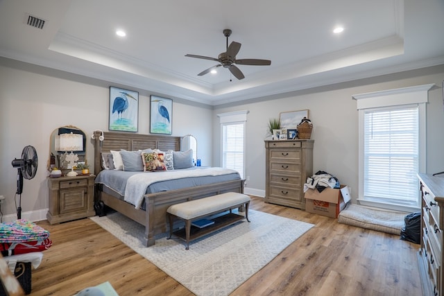 bedroom featuring a tray ceiling, multiple windows, ceiling fan, and light hardwood / wood-style flooring