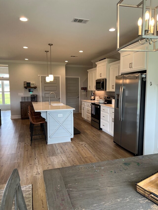 kitchen with white cabinetry, hanging light fixtures, dark wood-type flooring, a kitchen island with sink, and appliances with stainless steel finishes