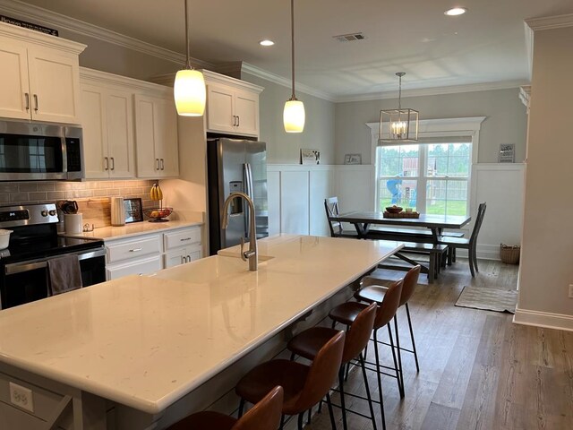 kitchen with a center island with sink, white cabinets, appliances with stainless steel finishes, decorative light fixtures, and dark hardwood / wood-style flooring