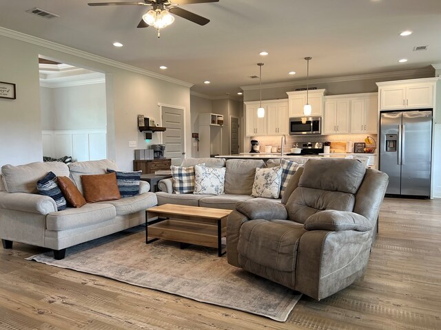 living room with light wood-type flooring, ceiling fan, crown molding, and sink