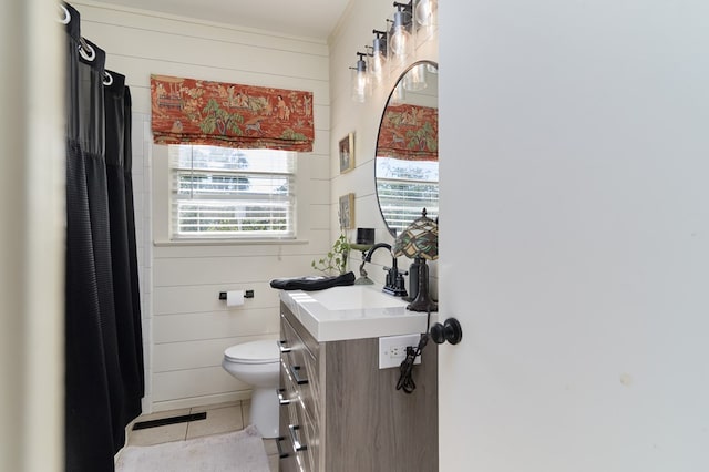 bathroom featuring tile patterned flooring, vanity, wooden walls, and toilet