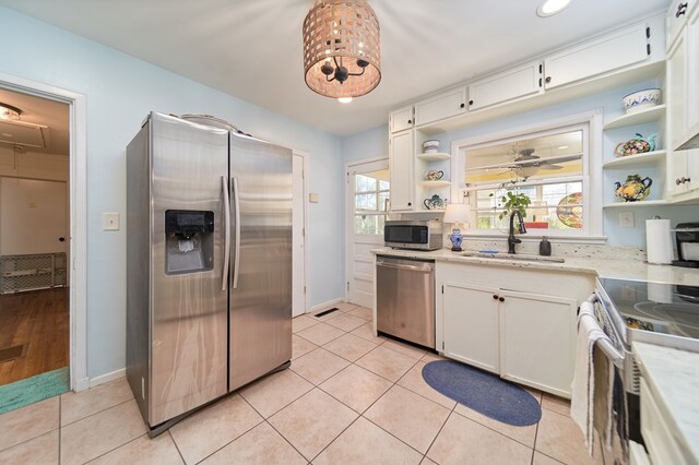 kitchen with appliances with stainless steel finishes, sink, white cabinets, light tile patterned floors, and a healthy amount of sunlight