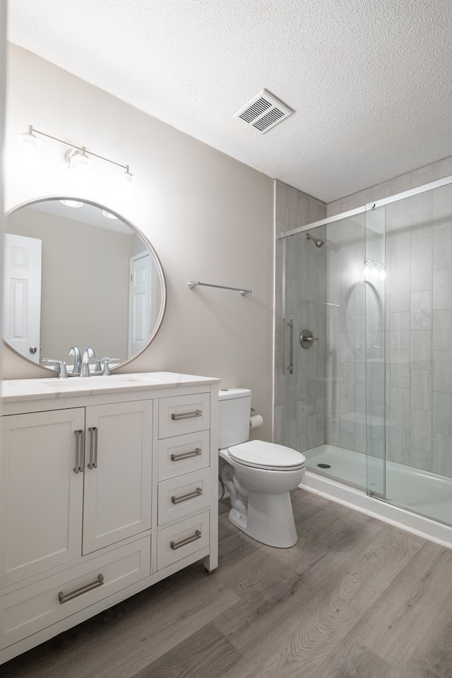 bathroom with walk in shower, vanity, a textured ceiling, wood-type flooring, and toilet