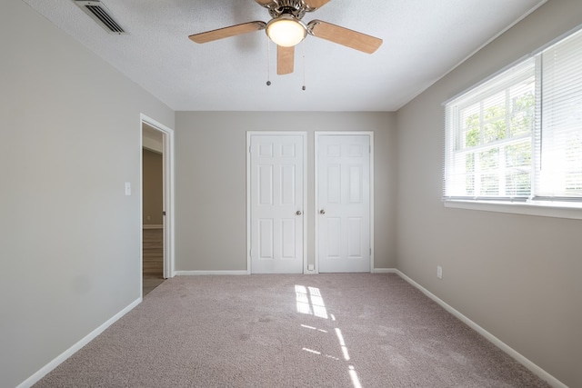 unfurnished bedroom featuring a textured ceiling, carpet floors, ceiling fan, and multiple closets