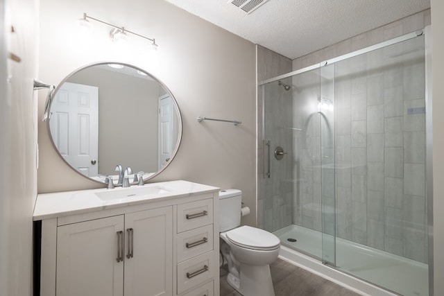 bathroom featuring walk in shower, vanity, a textured ceiling, hardwood / wood-style flooring, and toilet