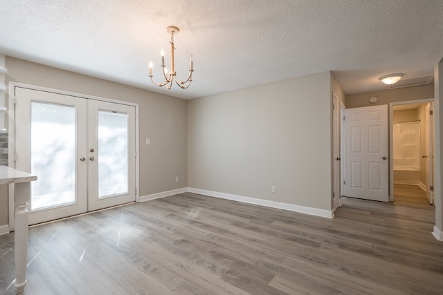 unfurnished dining area featuring french doors, a textured ceiling, an inviting chandelier, and hardwood / wood-style floors