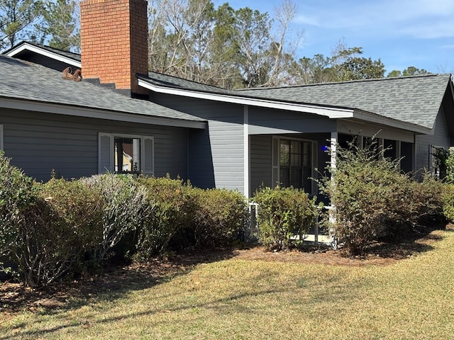 view of property exterior featuring roof with shingles, a yard, and a chimney