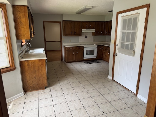 kitchen featuring light tile patterned floors, under cabinet range hood, a sink, light countertops, and white electric range oven