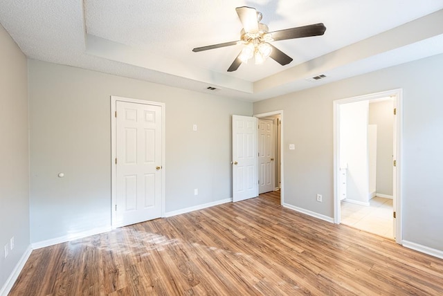 unfurnished bedroom featuring a textured ceiling, light wood-type flooring, ensuite bathroom, and ceiling fan