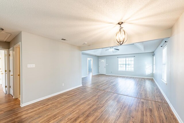 spare room featuring ceiling fan with notable chandelier, wood-type flooring, and a textured ceiling