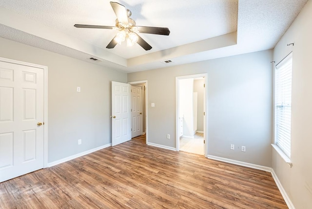 unfurnished bedroom featuring ceiling fan, wood-type flooring, a textured ceiling, and a tray ceiling