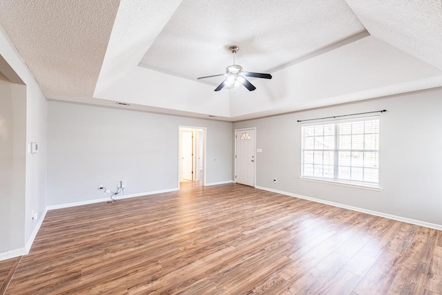 unfurnished room with a raised ceiling, ceiling fan, wood-type flooring, and a textured ceiling