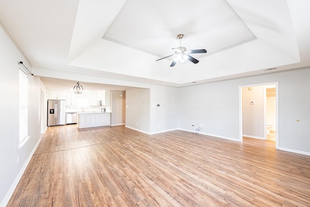 unfurnished living room with a raised ceiling, a barn door, ceiling fan, and light wood-type flooring