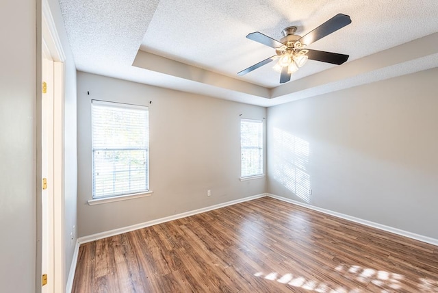 empty room with hardwood / wood-style floors, ceiling fan, a raised ceiling, and a textured ceiling