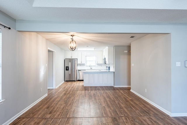 kitchen with appliances with stainless steel finishes, dark hardwood / wood-style flooring, a textured ceiling, white cabinets, and hanging light fixtures