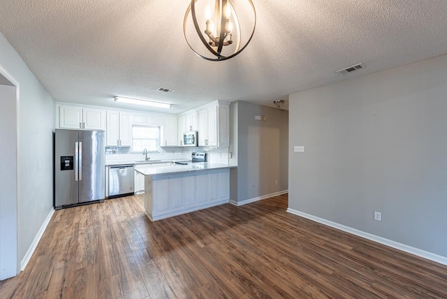 kitchen with kitchen peninsula, stainless steel appliances, dark wood-type flooring, sink, and white cabinetry