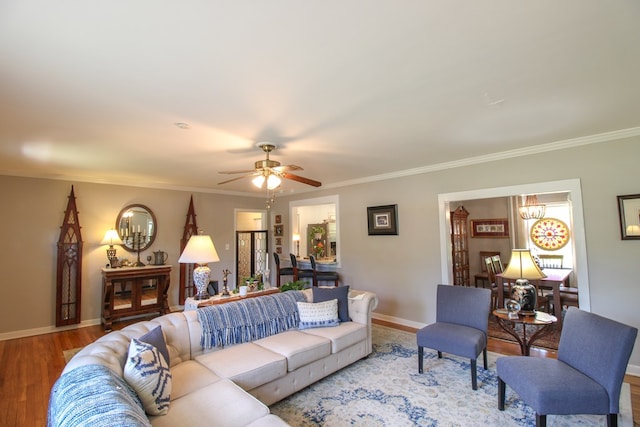 living room featuring baseboards, ornamental molding, wood finished floors, and ceiling fan with notable chandelier