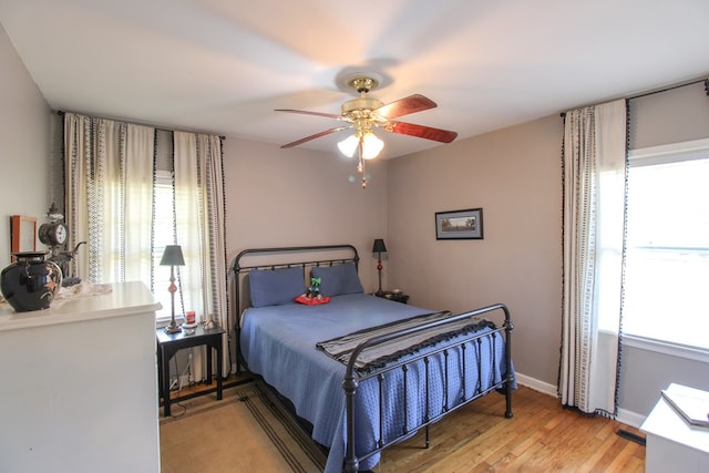 bedroom featuring light wood-style floors, baseboards, multiple windows, and a ceiling fan