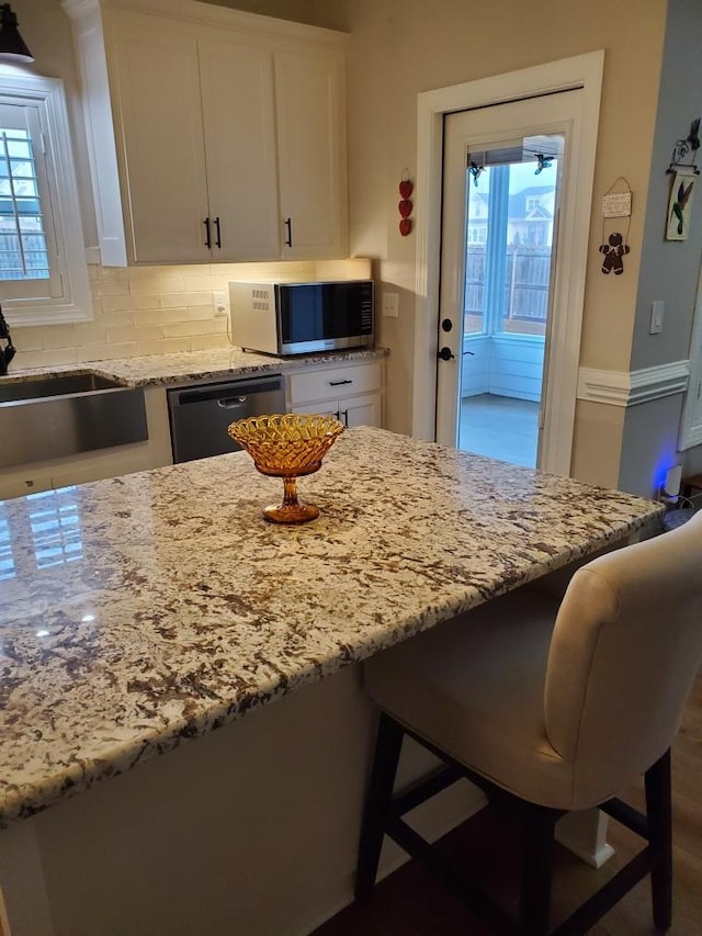 kitchen with plenty of natural light, white cabinetry, a kitchen breakfast bar, stainless steel appliances, and light stone countertops