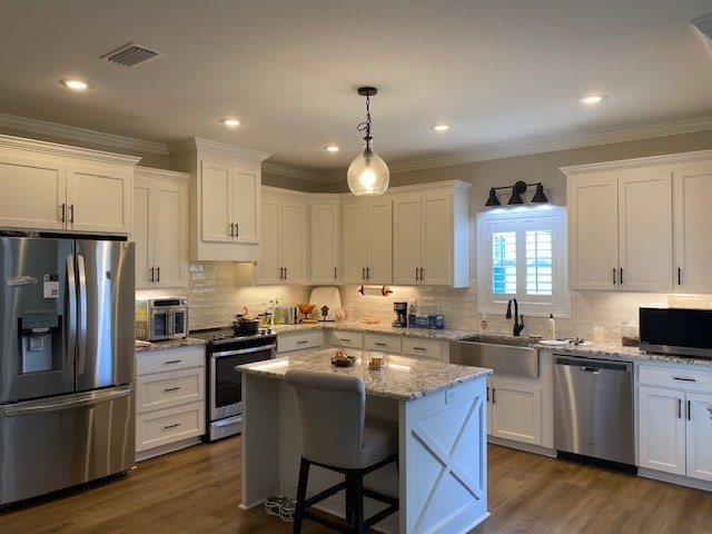 kitchen featuring pendant lighting, sink, stainless steel appliances, a center island, and white cabinets