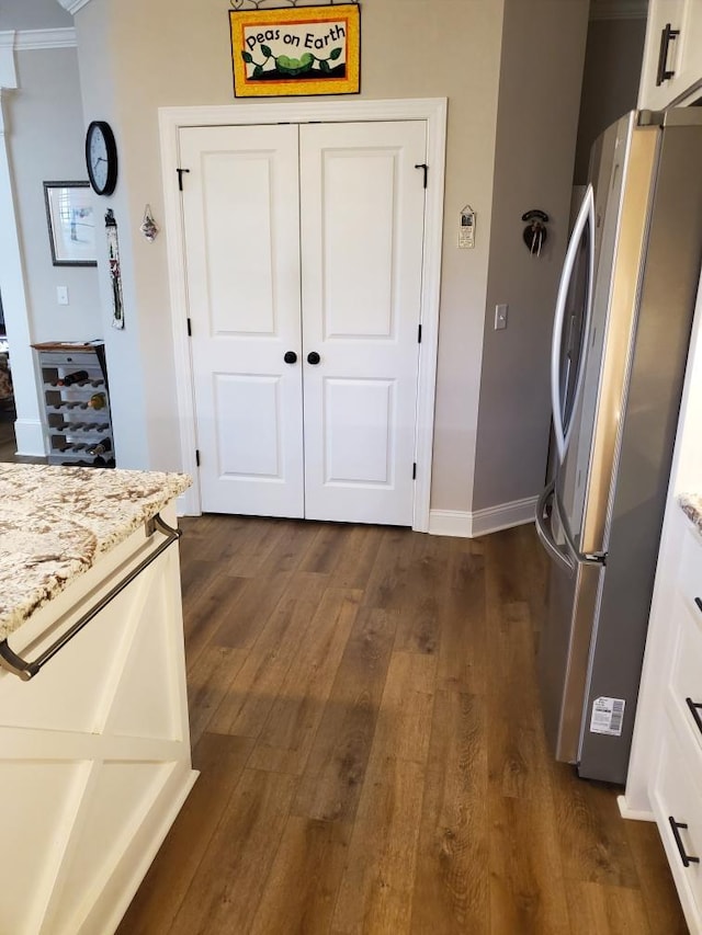 kitchen featuring stainless steel fridge, white cabinetry, dark hardwood / wood-style floors, ornamental molding, and light stone countertops