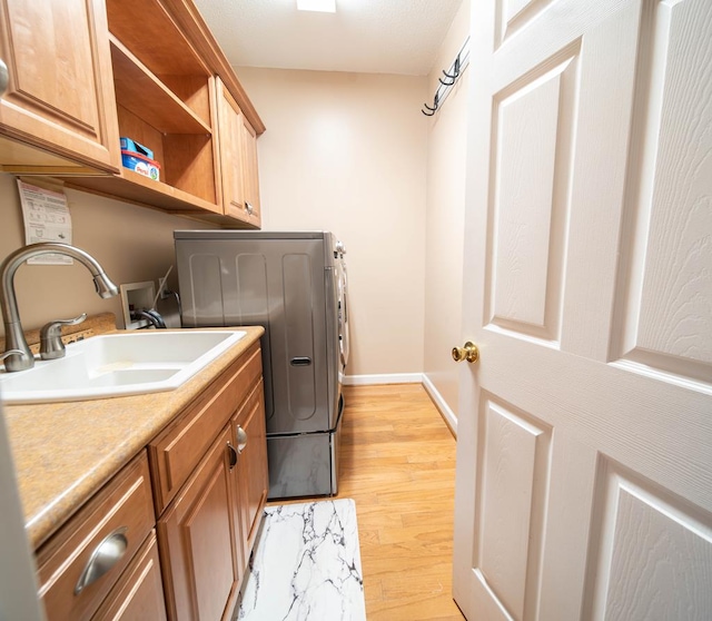 clothes washing area with washer / dryer, sink, cabinets, and light wood-type flooring