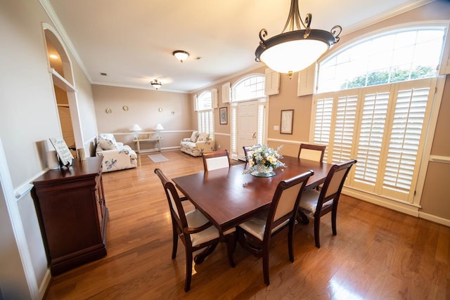 dining area featuring wood-type flooring, ornamental molding, and a healthy amount of sunlight