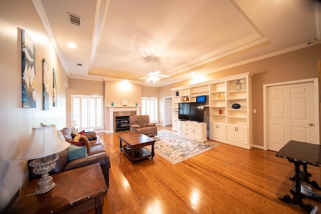 living room with wood-type flooring, a raised ceiling, ceiling fan, and crown molding