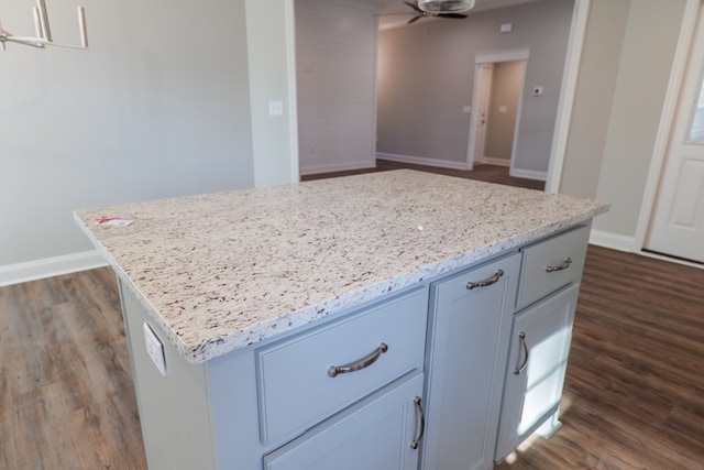 kitchen with ceiling fan, a kitchen island, dark hardwood / wood-style floors, and light stone countertops