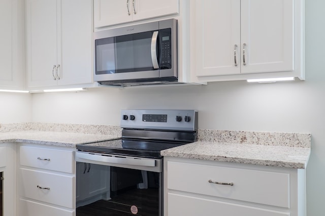 kitchen featuring appliances with stainless steel finishes, light stone counters, and white cabinetry