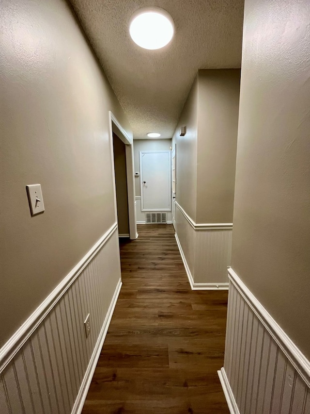 hallway with an upstairs landing, a textured ceiling, visible vents, and wood finished floors