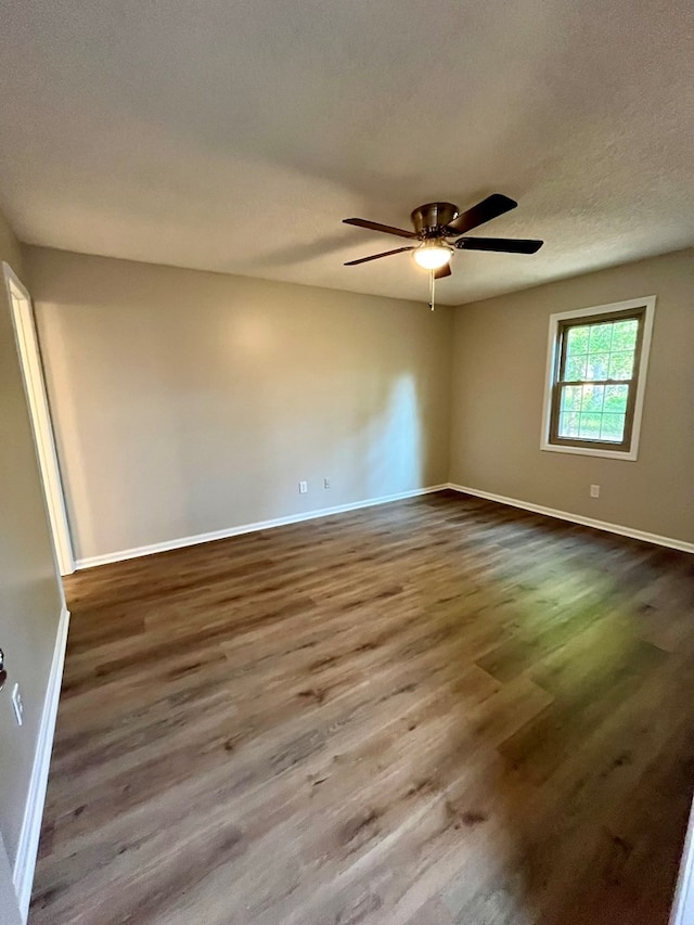 empty room with baseboards, a ceiling fan, and dark wood-style floors