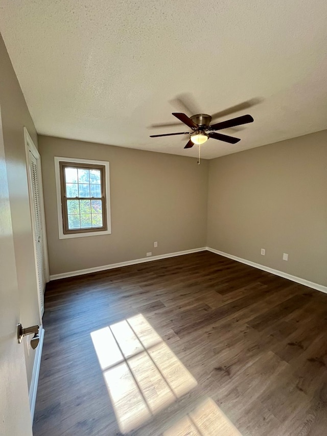 empty room with a textured ceiling, baseboards, dark wood-type flooring, and a ceiling fan