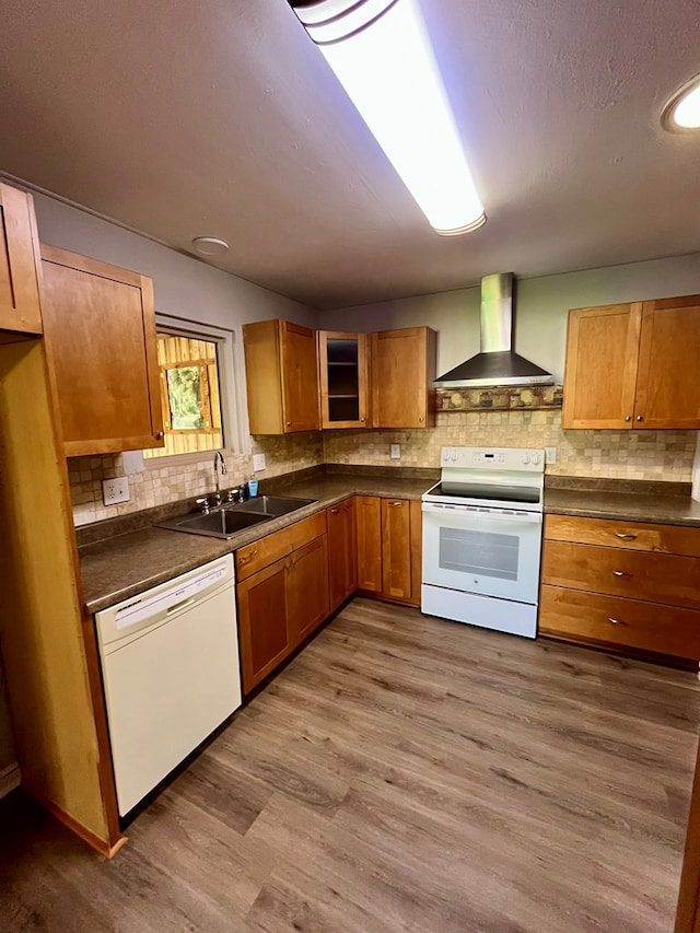 kitchen featuring white appliances, a sink, wood finished floors, wall chimney range hood, and dark countertops