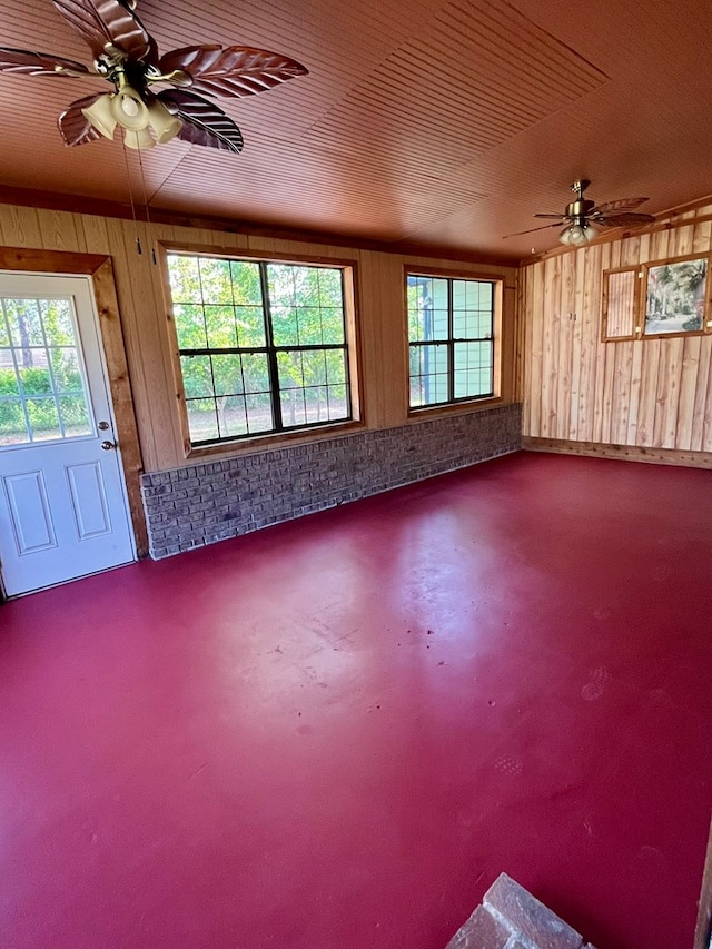 spare room featuring ceiling fan, wood walls, and concrete flooring
