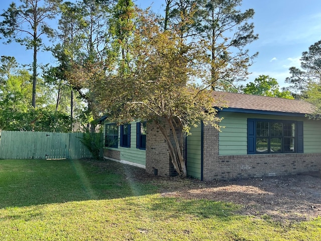 view of side of home featuring a lawn, brick siding, and fence