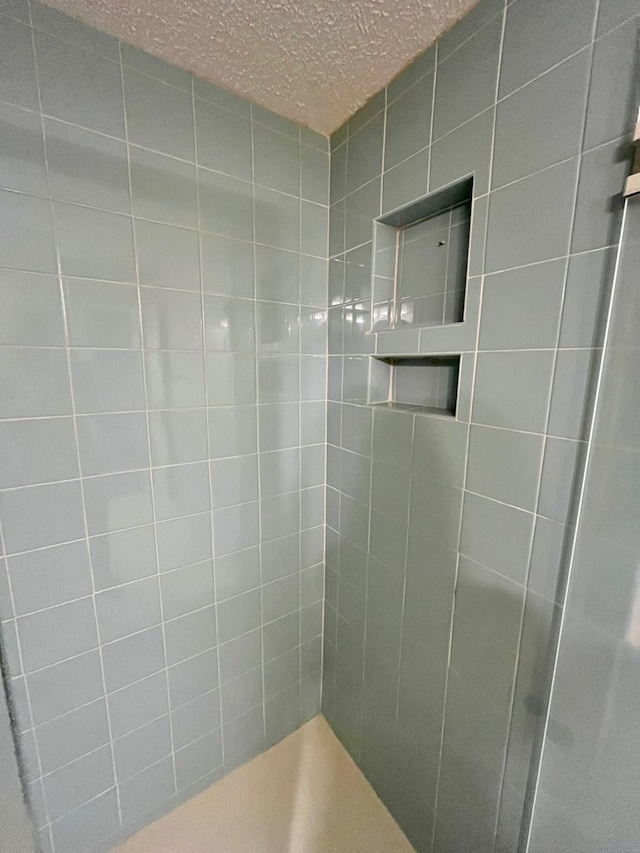 full bath featuring a textured ceiling and tiled shower