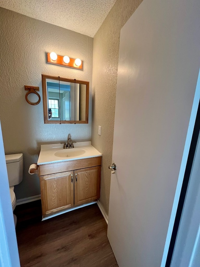 bathroom with a textured ceiling, toilet, vanity, wood finished floors, and a textured wall