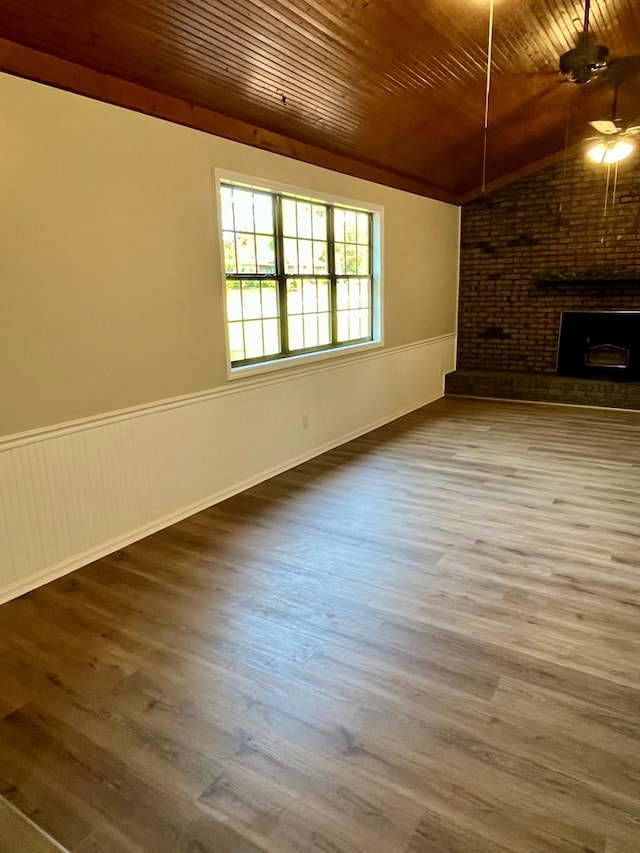 unfurnished living room with lofted ceiling, a wainscoted wall, wood finished floors, wooden ceiling, and a brick fireplace
