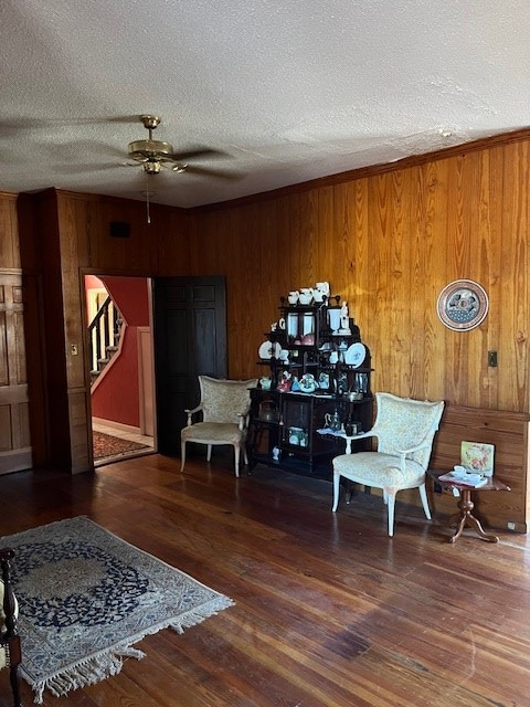 living area featuring ceiling fan, dark hardwood / wood-style floors, a textured ceiling, and wood walls