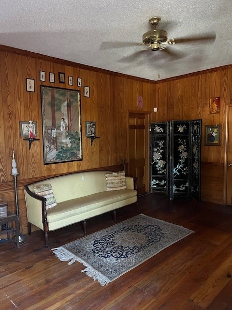 living area with ceiling fan, wooden walls, dark hardwood / wood-style floors, and a textured ceiling