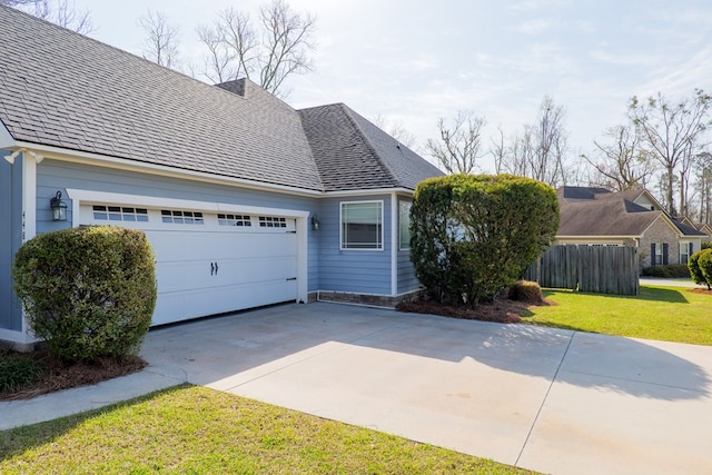 view of home's exterior with concrete driveway, roof with shingles, an attached garage, fence, and a yard