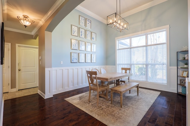 dining area featuring wood-type flooring, arched walkways, crown molding, and wainscoting