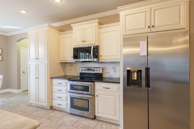 kitchen with arched walkways, stainless steel appliances, cream cabinetry, ornamental molding, and tasteful backsplash