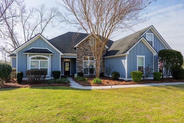 view of front of house with stone siding, a front lawn, board and batten siding, and roof with shingles