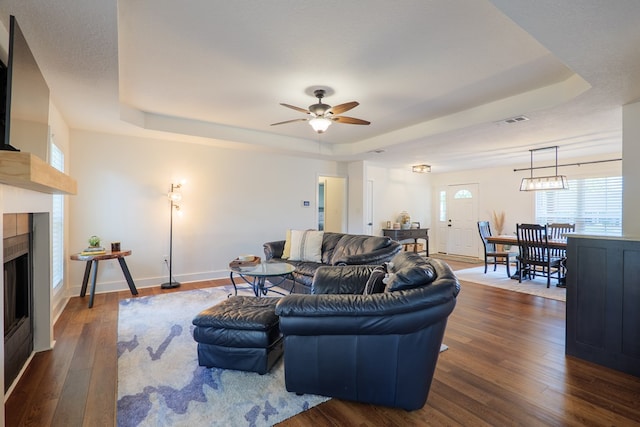 living room featuring a tile fireplace, visible vents, a tray ceiling, and dark wood-style floors