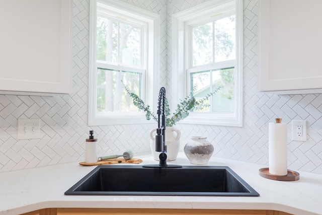 interior details featuring light stone counters, white cabinetry, backsplash, and a sink